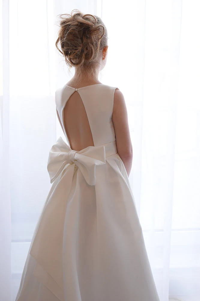 Ivory satin flower girl dress with open back cutout, single button closure and large satin bow, full skirt with train
