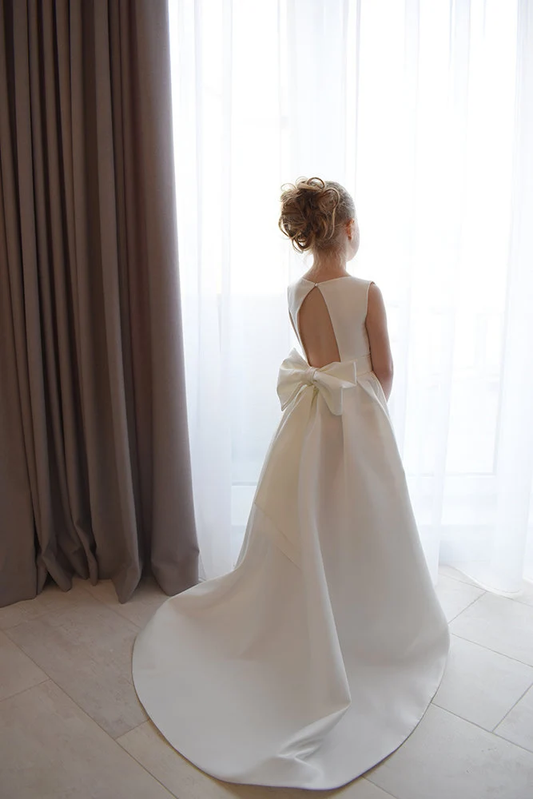 Ivory satin flower girl ball gown with open V-back, large satin bow and floor-length train, interior setting