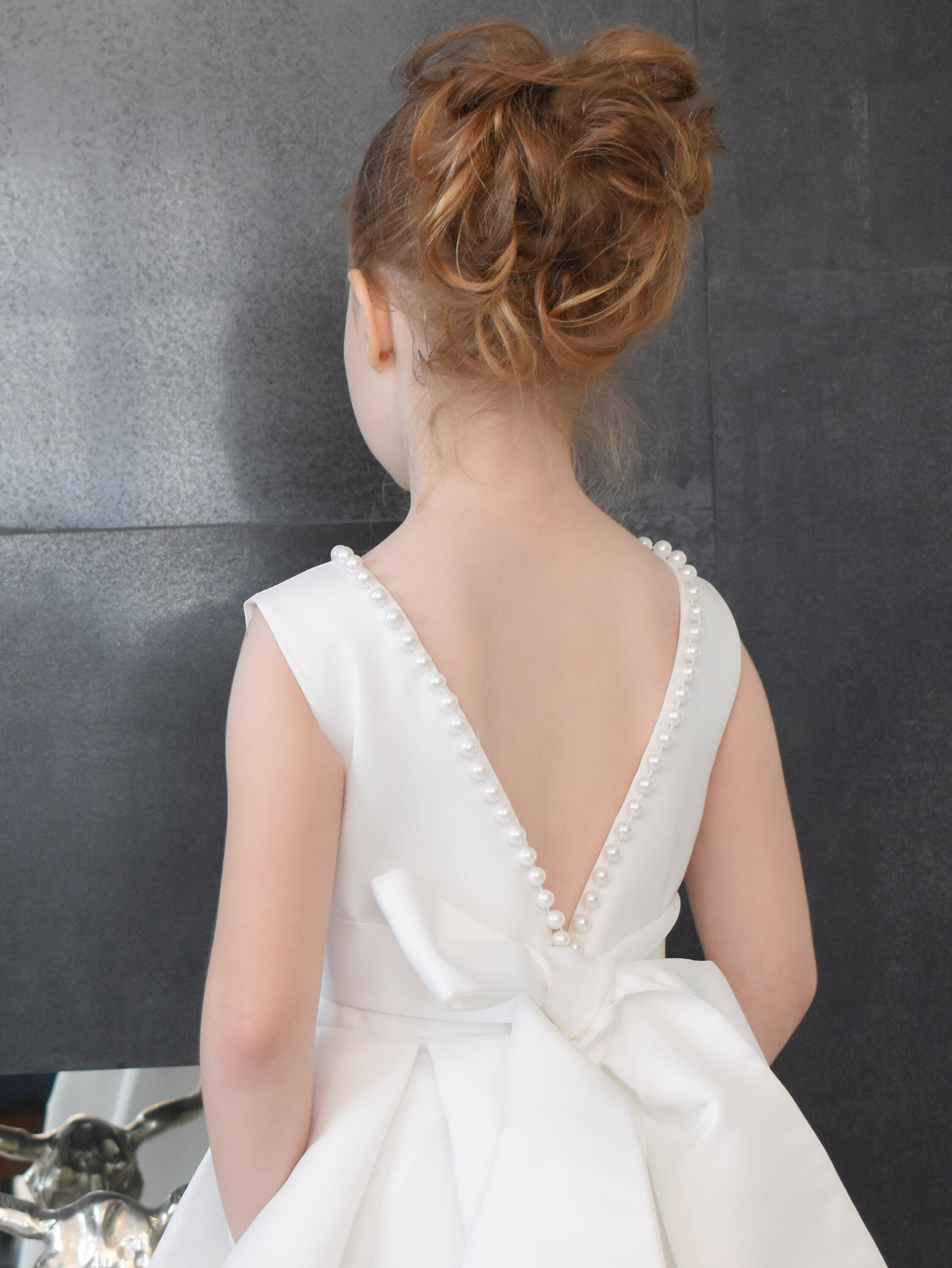 Close-up of ivory satin flower girl dress V-back with pearl trim along edges and satin bow at waist