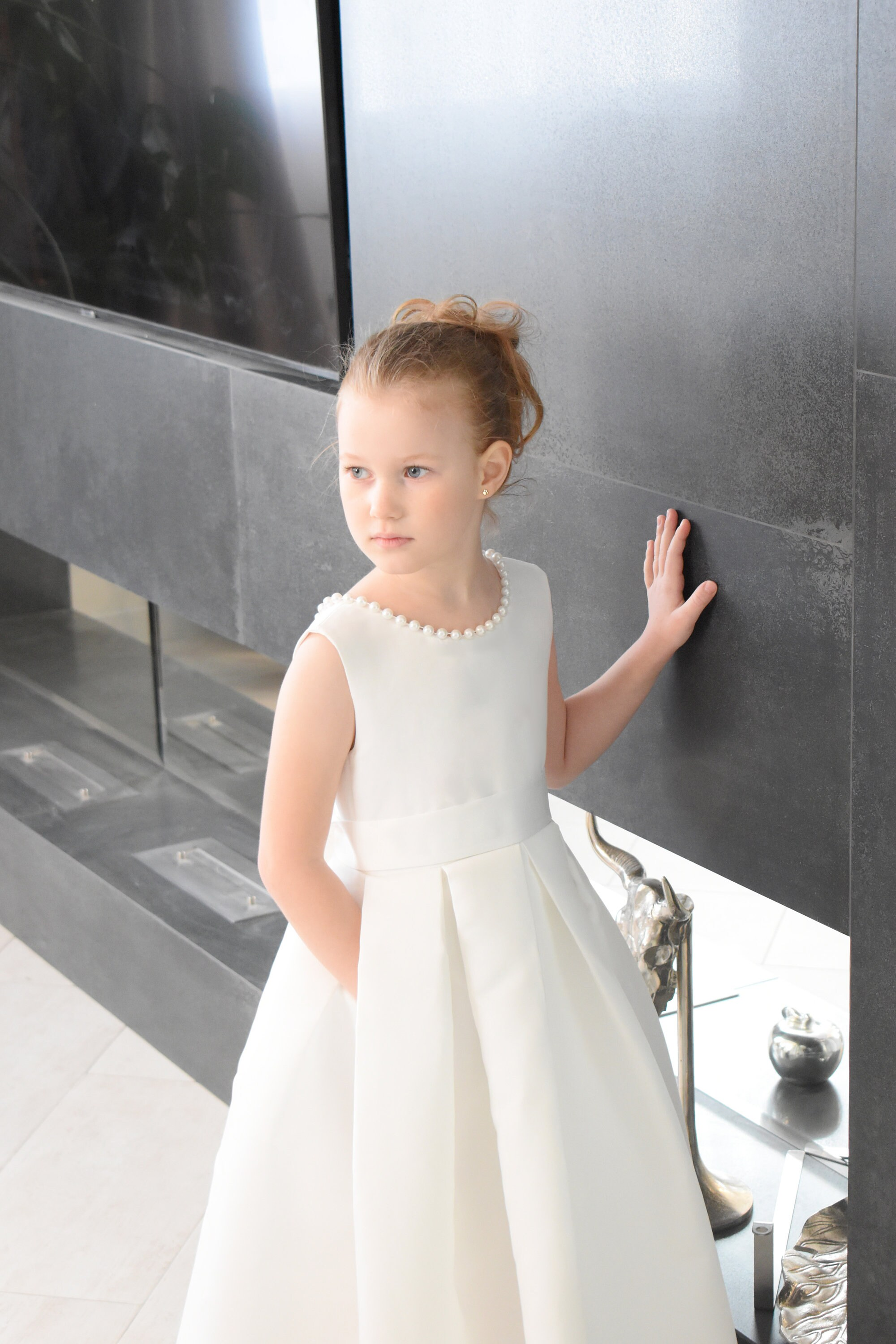 Ivory satin flower girl dress with pearl neckline trim, structured bodice and box-pleated ball gown skirt