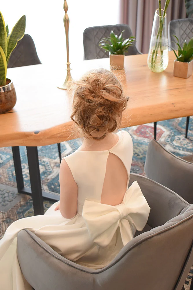 Ivory satin flower girl dress back view showing open cutout with button closure and large structured satin bow