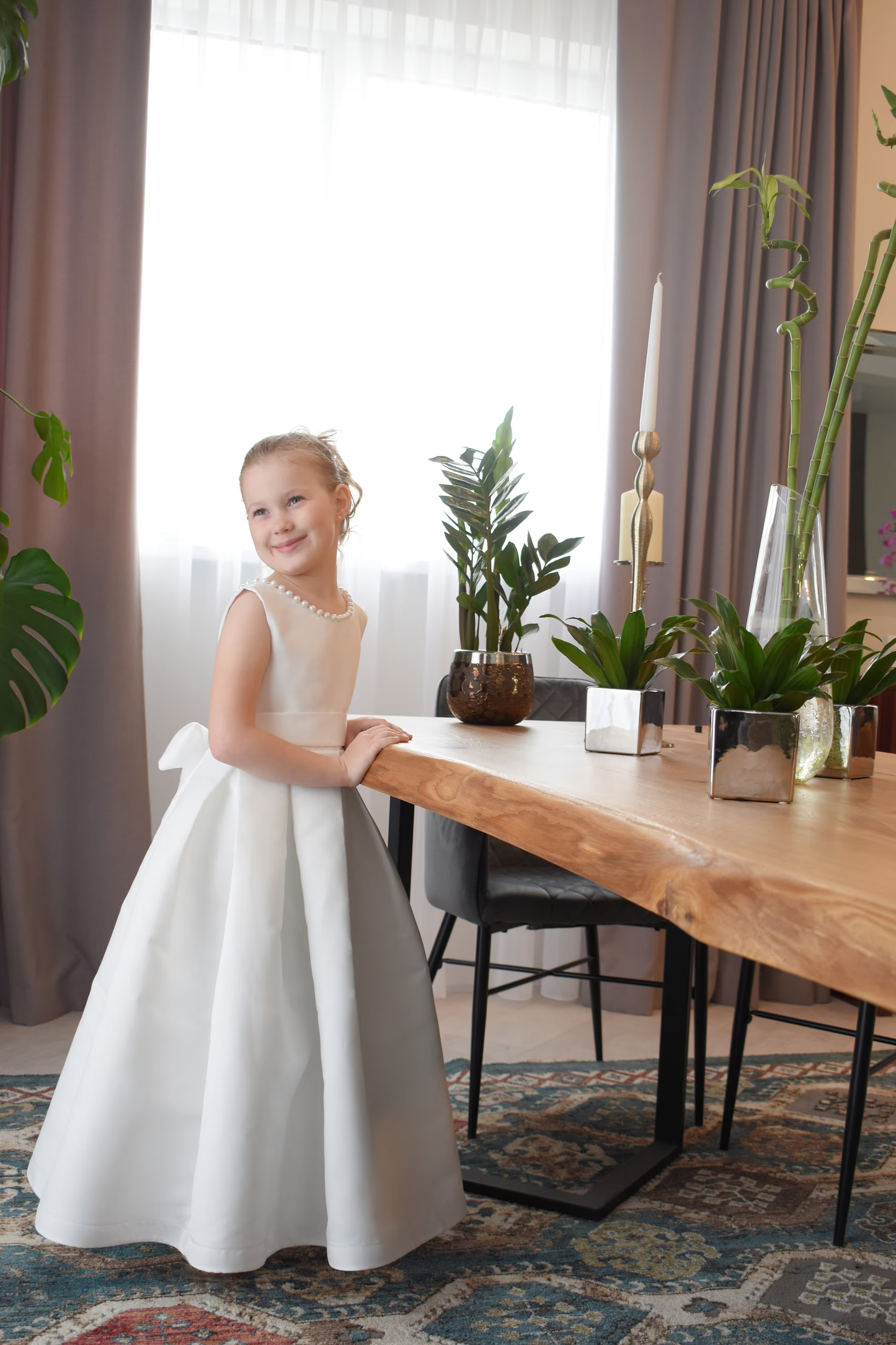 Ivory satin flower girl dress with pearl neckline, narrow satin waistband and full ball gown skirt, bright interior setting