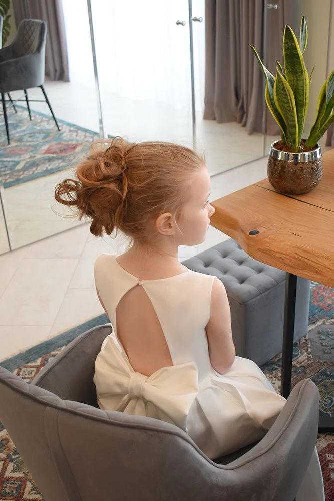 Close-up of ivory satin flower girl dress open back with single button and large satin bow at waist