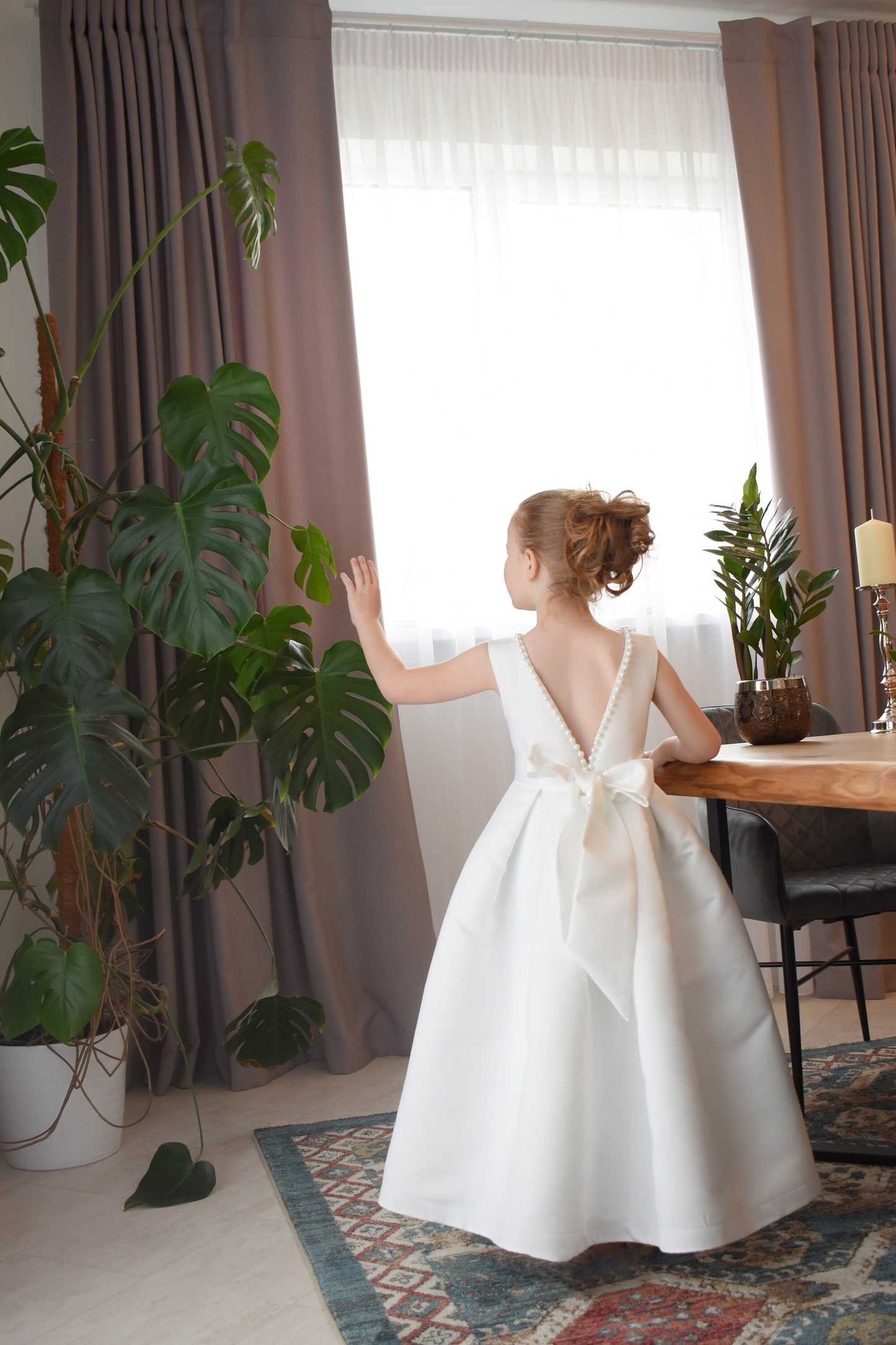 Ivory satin flower girl dress with pearl-trimmed V-back and satin bow, full ball gown skirt, interior setting